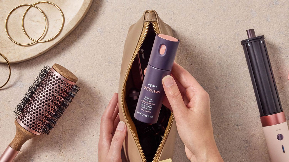 Model holding the Dyson Chitosan Multi-use styling spray in a makeup bag.