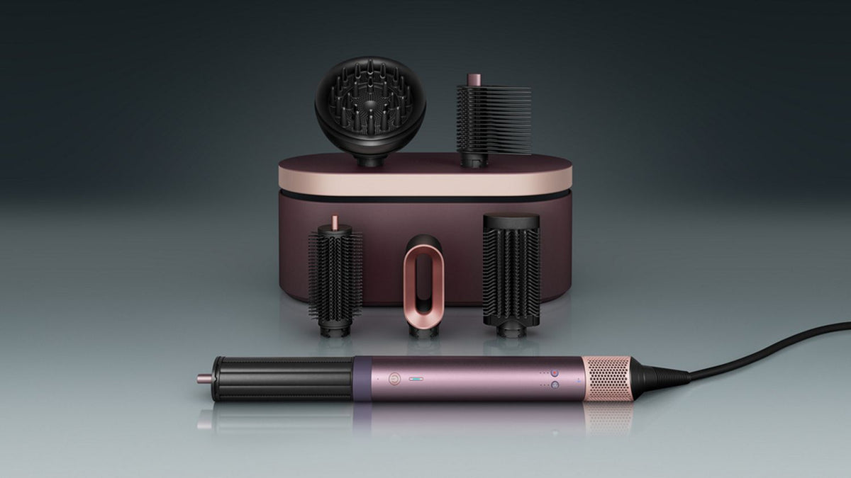 The Dyson Airwrap Co-anda2x multi-styler and dryer with the Wave+Curl diffuser 2x attachment next to a coily haired model.