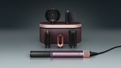 The Dyson Airwrap Co-anda2x multi-styler and dryer with the Wave+Curl diffuser 2x attachment next to a coily haired model.