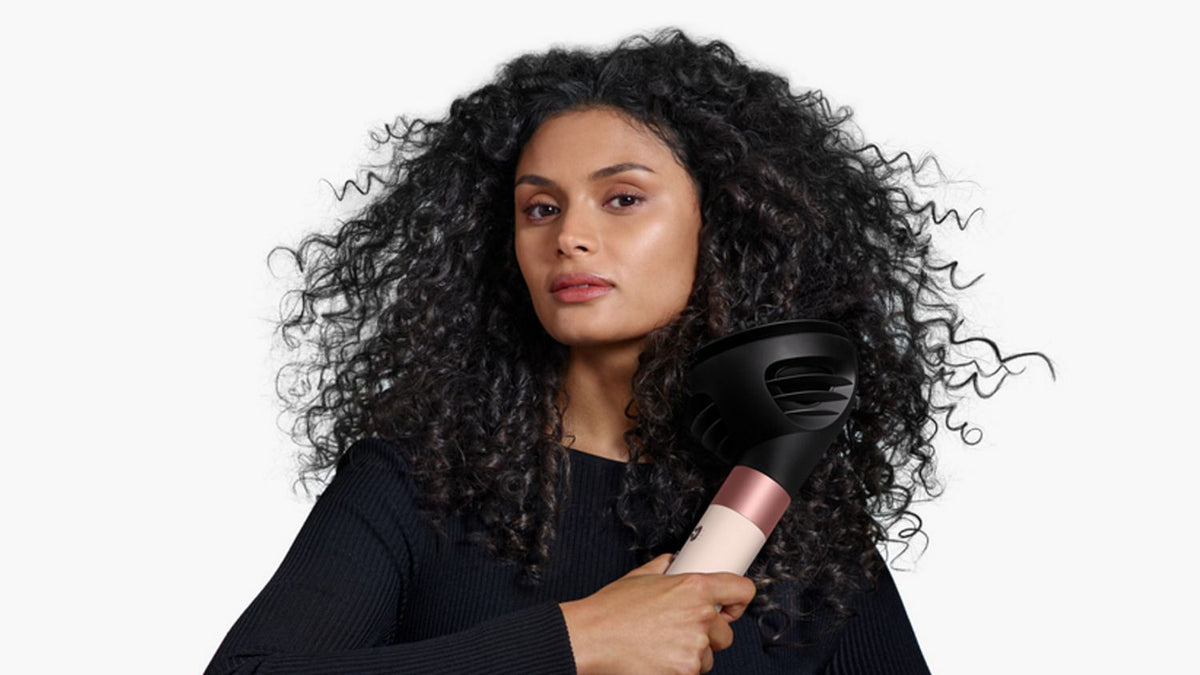 A woman enhances her natural curls with the Dyson Airwrap ID and the Wave+Curl diffuser in Dome mode.