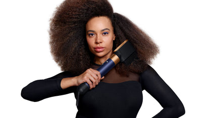 A dark-haired model defines her natural curls using the Dyson Airwrap i.d. multi-styler and dryer and the Wave+Curl diffuser.